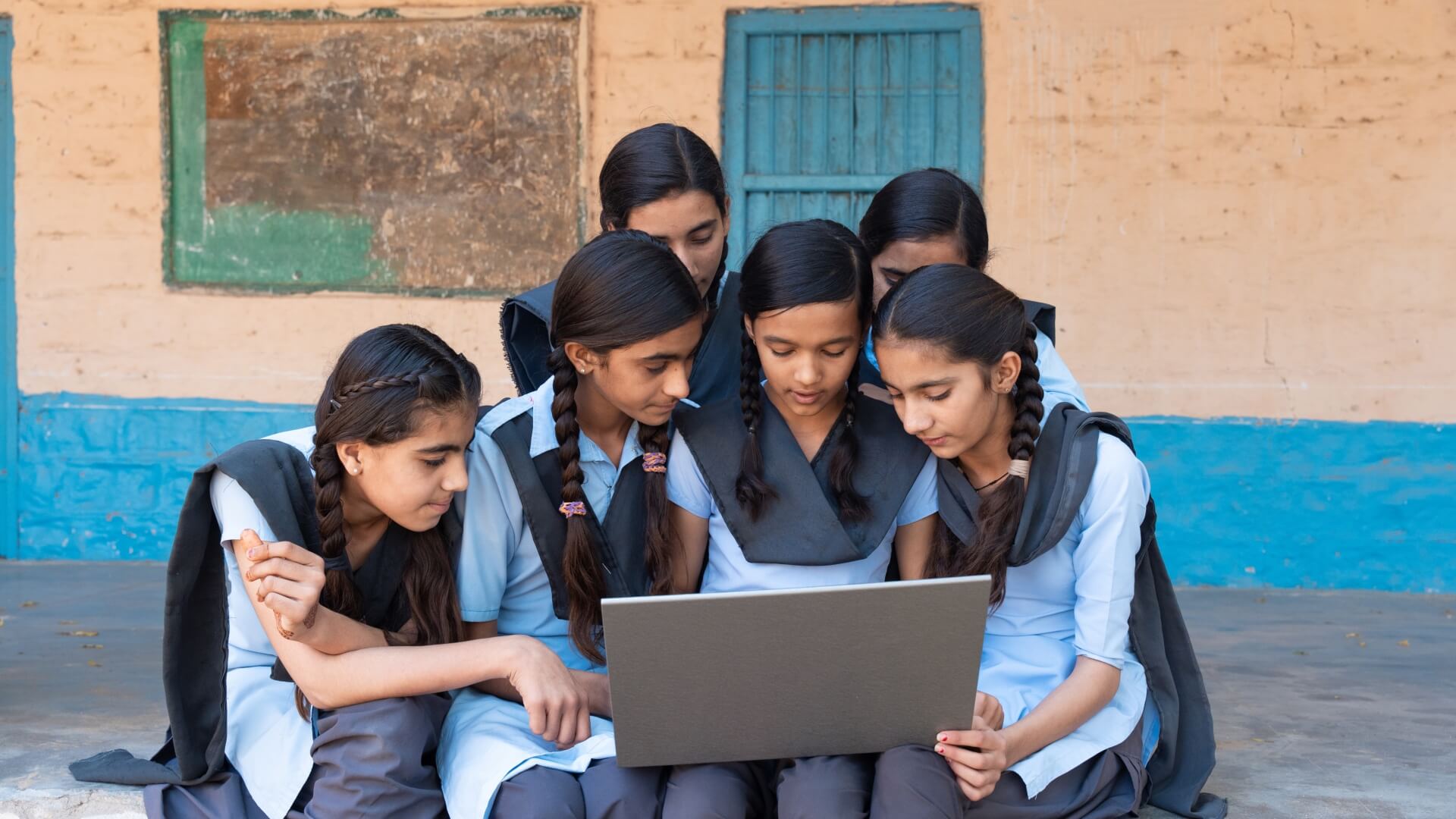 Group of Indian girls in school uniforms sitting together for online learning looking at a laptop